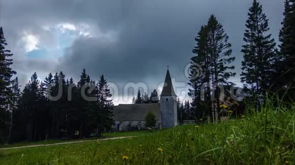 时间流逝高山村教堂和草地上的戏剧性的云彩和前面的鲜花视频的预览图