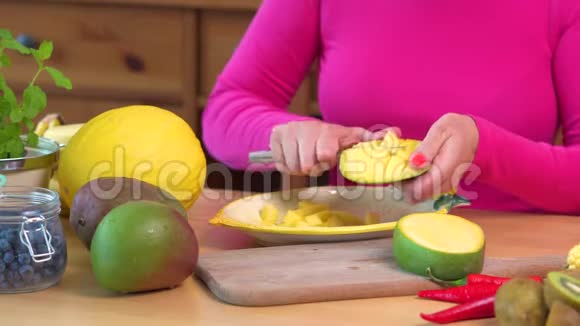 穿着粉红色上衣的女人在桌子上切一个多汁的黄色芒果视频的预览图