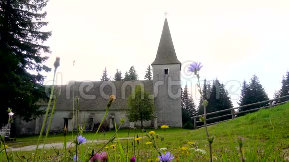 时间流逝高山教堂和草地上的戏剧性的云彩和前面的鲜花视频的预览图