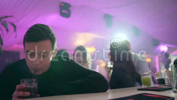 孤独而沮丧的家伙在酒吧柜台后面喝着酒在灯光的背景下喝着鸡尾酒视频的预览图