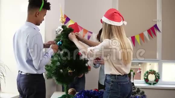 幸福微笑的办公室职员装饰戴着新年帽和鹿的小人造圣诞树画像视频的预览图