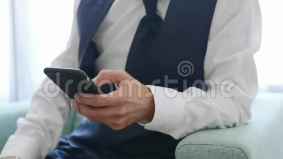 穿西装的男人手拿智能手机坐在扶手椅上视频的预览图