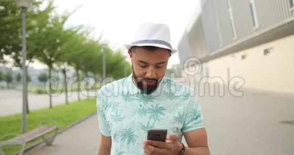 戴着白帽子的漂亮非洲男人正在手机上聊天和浏览他正在看摄像机视频的预览图