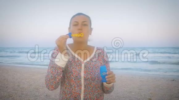 在一个刮风的日子里穿着五颜六色西装的女孩在海滩上吹着肥皂泡视频的预览图