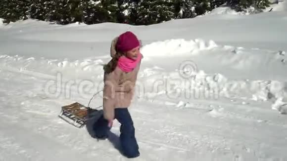 一个快乐的女孩在冬天的山上穿过一片雪林她在笑她把雪橇拉到身后视频的预览图