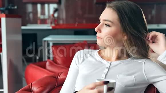 年轻女子坐在椅子上在红色时髦的公寓里喝咖啡视频的预览图