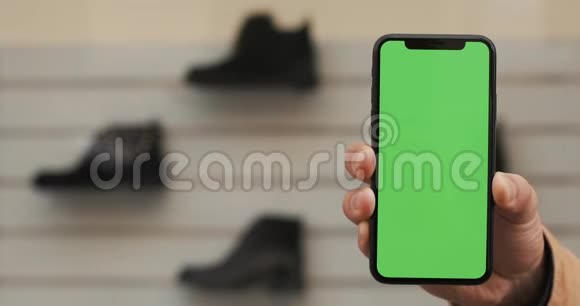 男性手拿黑色智能手机绿色屏幕在商店与鞋背景大屏幕铬钥匙关闭视频的预览图