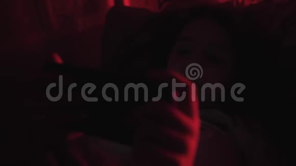 小女孩躺在黑暗的毯子下看着智能手机房间里有红灯视频的预览图