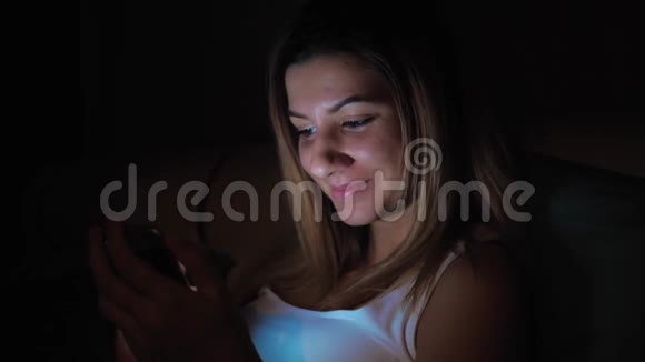 在睡觉前使用智能手机的黑暗中的女人脸从屏幕上发光视频的预览图