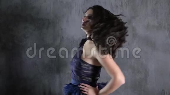 穿着晚礼服在灰墙背景上化妆的迷人女孩挥舞着头发视频的预览图