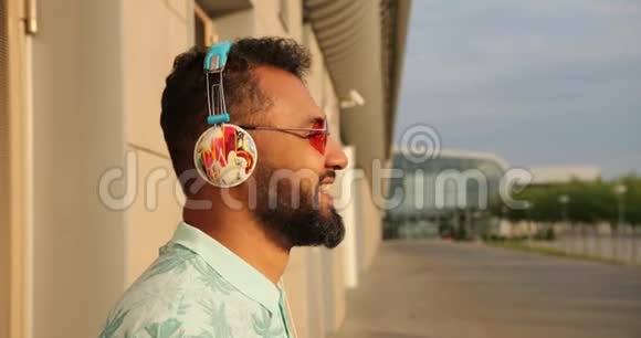 这位年轻快乐的非洲男人戴着粉红色太阳镜和耳机在机场附近笑的情绪侧面肖像4k视频的预览图