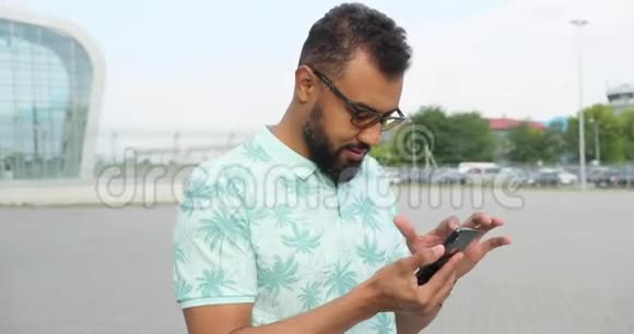 自信迷人的戴眼镜的非洲男人正在玻璃建筑附近的手机上浏览和发短信旋转视频的预览图