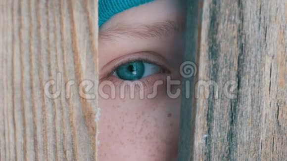一个充满泪水的十几岁男孩的一只不寻常的绿松石眼睛透过门口或栅栏的一个缝隙直接看向视频的预览图