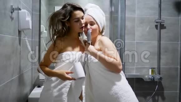 穿着白色毛巾的漂亮女人在淋浴房的背景下跳舞唱歌梳头和淋浴头视频的预览图