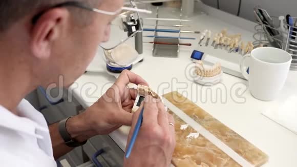 牙科植入物的制作男性专家用刷子把白色陶瓷釉涂在人工下巴上视频的预览图