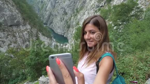 一个女旅行者在一部智能手机上的风景如画的山峡谷中自拍视频的预览图