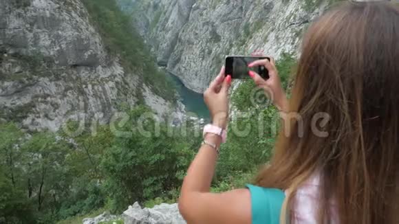 女游客在智能手机上拍摄景区峡谷图片视频的预览图