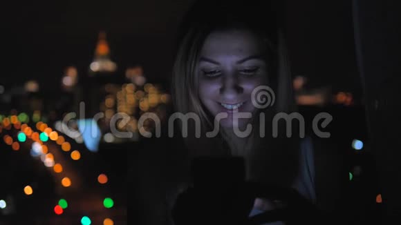 站在窗口的黑暗中的女人使用从屏幕4k照亮的移动脸视频的预览图