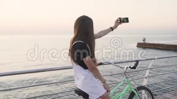 日出或日落时在海边骑自行车自拍的年轻迷人女子视频的预览图