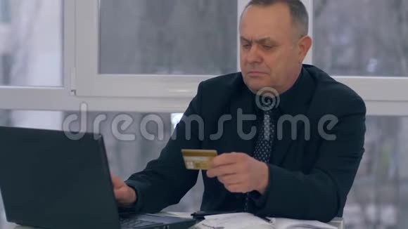 在网上购买养老金的商人一手拿着信用卡在现代的办公室里使用笔记本电脑视频的预览图