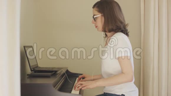 年轻女子用手提电脑和耳机弹钢琴视频的预览图