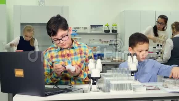 学校科学概念孩子们在学校实验室里看显微镜学习生物学化学特写镜头视频的预览图