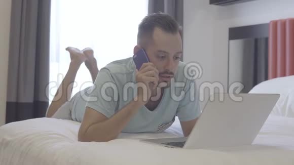 在线商务男人在笔记本电脑上工作时打电话躺在床上视频的预览图