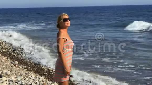 穿着裙子戴太阳镜的年轻女子在海边散步视频的预览图