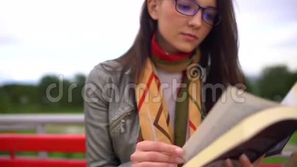 夏天带着眼镜的年轻美女坐在公园外面的长凳上看书把脸贴紧4视频的预览图