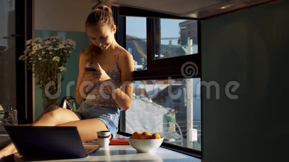 金发女郎在窗台上的智能手机上读信息视频的预览图