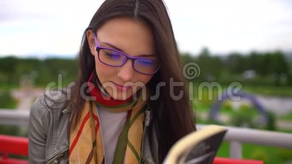 夏天带着眼镜的年轻美女坐在公园外面的长凳上看书把脸贴紧4视频的预览图