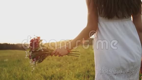 穿着白色连衣裙的女人在夏天的傍晚带着一束野花走进田野视频的预览图