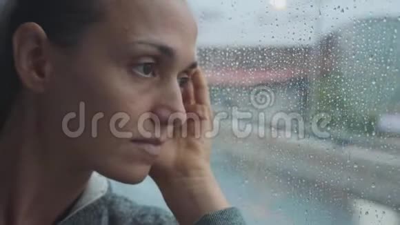 年轻悲伤的女人在乘公共汽车旅行时看着潮湿的窗户的肖像视频的预览图