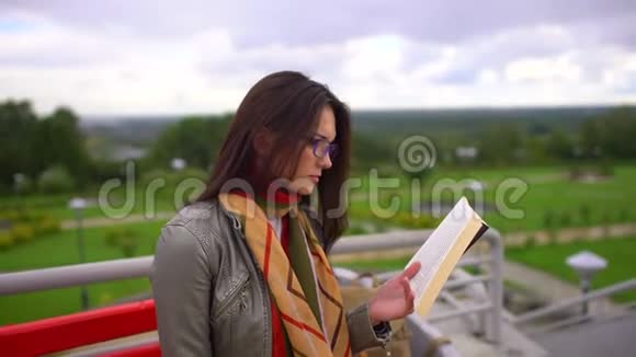 夏天带着眼镜的年轻美女坐在公园外面的长凳上看书4千克视频的预览图