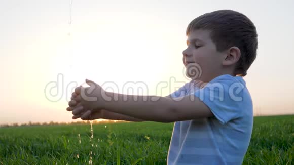 在黎明的背景天空中小男孩洗手水在绿野中飞溅视频的预览图