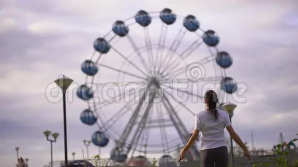 年轻女子在摩天轮背景下在公园里跳绳视频的预览图