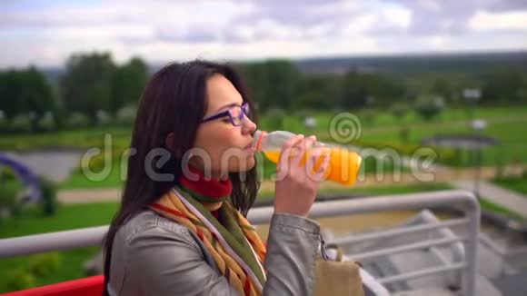 在夏日公园户外喝橙汁的年轻美女4千视频的预览图