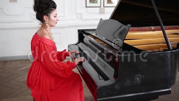 优雅的女人穿着红色长裙戴着昂贵的珠宝坐在房间里弹钢琴视频的预览图