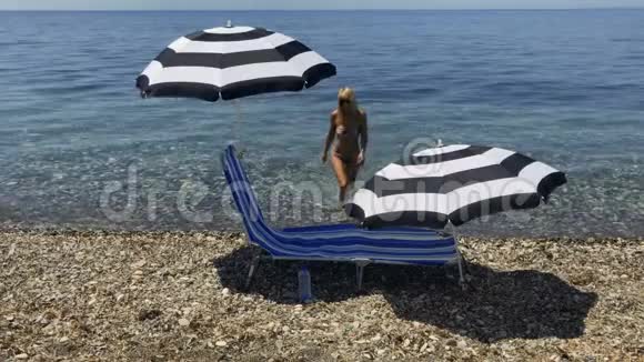 穿着比基尼的美丽成年女子躺在海滩的躺椅上喝水视频的预览图
