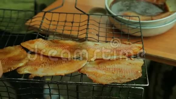 一个女人手把一块腌制的鱼放在烤架上视频的预览图