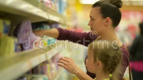 可爱的女孩带着棒棒糖坐在超市手推车里妈妈在后台选择湿巾视频的预览图