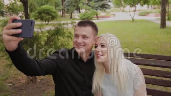 恋爱中的幸福夫妇坐在城市公园的长凳上打电话自拍视频的预览图