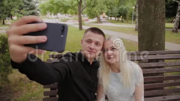 恋爱中的幸福夫妇坐在城市公园的长凳上打电话自拍视频的预览图
