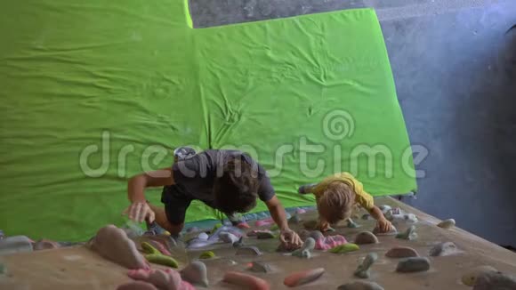 一个年轻的攀岩教练教小男孩如何在一个巨石攀岩馆里爬墙视频的预览图