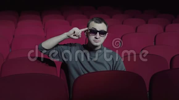 一个单身男人坐在黑暗电影院里舒适的红椅子上在她的庙里扭着她的手指视频的预览图