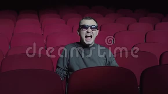 情绪化的单身男人在黑暗的电影院里对着舒适的红色椅子尖叫视频的预览图