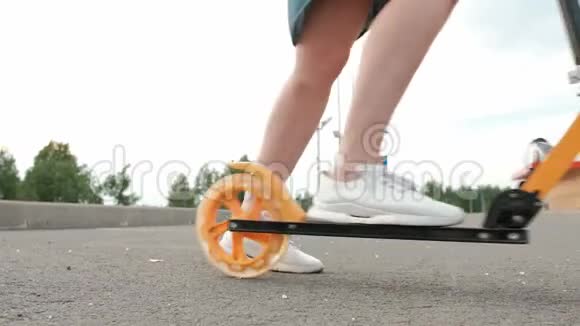 漂亮的年轻女子穿着牛仔裙穿着白色运动鞋骑着一辆踢踏车穿过街道视频的预览图
