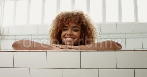 一幅黑发黑女人的画像她的卷发靠在游泳池边在镜头前观看视频的预览图