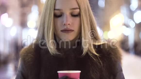 特写一个年轻女子在夜市街喝咖啡背景中的模糊灯光视频的预览图