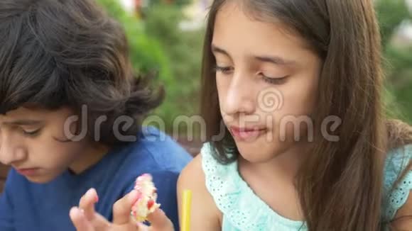 悲伤的男孩和十几岁的女孩坐在长凳上手里拿着新鲜和冰沙的眼镜吃甜甜圈和羊角面包视频的预览图